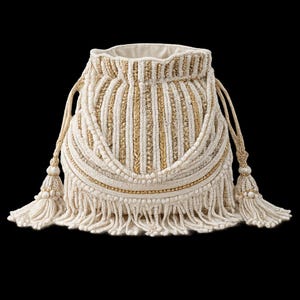 Può includere: Una pochette con coulisse color crema caratterizzata da strisce verticali in filo metallico dorato e cordoncino bianco testurizzato. La borsa è decorata con un inserto curvo, frange spesse sul bordo inferiore e due nappe laterali con perline.