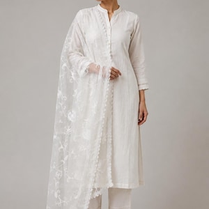 Pu&ograve; includere: Un completo bianco a tre pezzi composto da una tunica a maniche lunghe con colletto alla coreana e abbottonatura frontale, pantaloni dritti abbinati con bordo in pizzo sull'orlo e una dupatta bianca trasparente con ricami floreali.