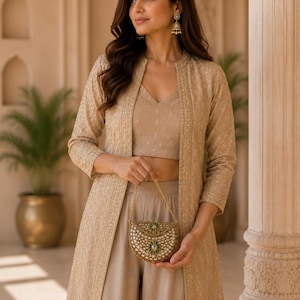 May include: A beige three-piece ensemble consisting of a sleeveless V-neck crop top, matching wide-leg trousers, and a long-sleeved open jacket with intricate embroidery. A small, semi-circular gold-toned clutch with green accents is held.