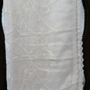 Pu&ograve; includere: Un tessuto bianco caratterizzato da intricati ricami floreali e paisley tono su tono. Il materiale ha un aspetto liscio e leggero ed &egrave; rifinito lungo un bordo verticale con un delicato bordo in pizzo bianco smerlato.