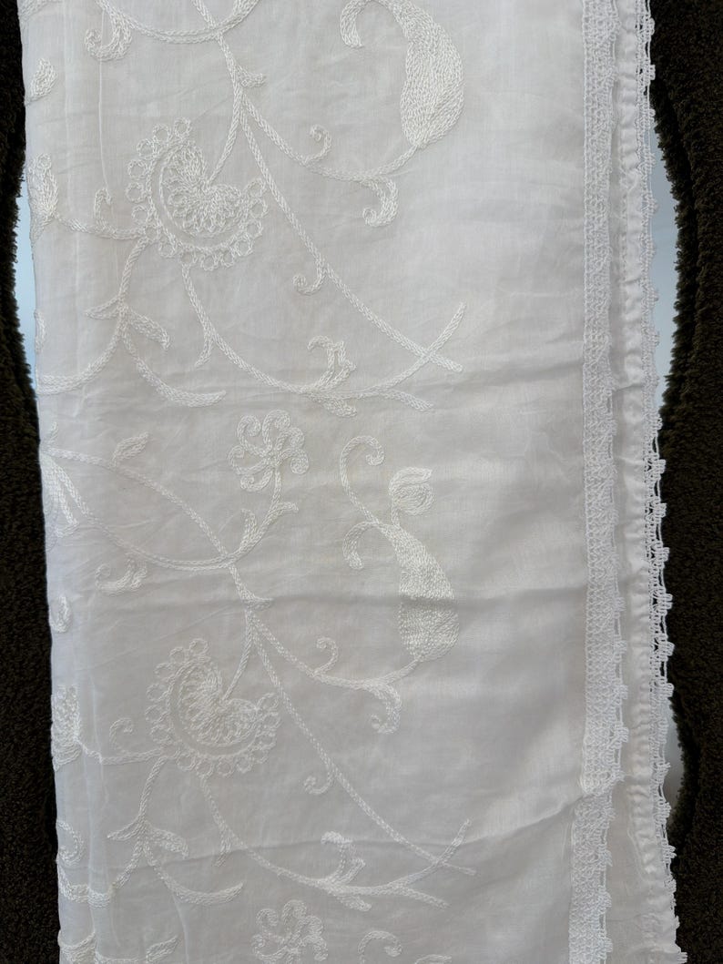 Pu&ograve; includere: Un tessuto bianco caratterizzato da intricati ricami floreali e paisley tono su tono. Il materiale ha un aspetto liscio e leggero ed &egrave; rifinito lungo un bordo verticale con un delicato bordo in pizzo bianco smerlato.