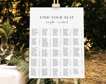 May include: A white wedding seating chart on an easel with the text "Find Your Seat Angela + Michael" at the top. The chart lists the names of guests and their assigned tables.
