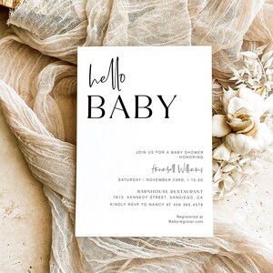 May include: A white baby shower invitation with the text "hello BABY" in black script font. The invitation includes details for a baby shower honoring Annabell Williams on Saturday, November 23rd at 3:50 PM at the Barnhouse Restaurant in San Diego, California. The invitation also includes an RSVP number and a website for the baby registry.