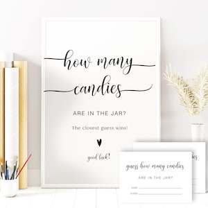 Könnte beinhalten: Ein weißes Schild mit schwarzem Text, der lautet: "how many candies ARE IN THE JAR? The closest guess wins! good luck!"  Eine weiße Karte mit schwarzem Text, der lautet: "guess how many candies ARE IN THE JAR? NAME GUESS" befindet sich unter dem Schild.
