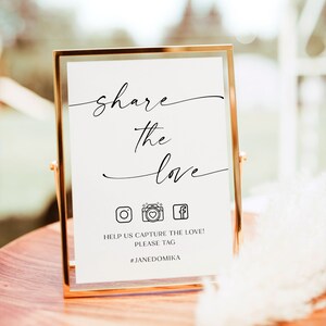 May include: A gold-framed sign with the text "share the love" and social media icons for Instagram, Facebook, and a camera. The text below the icons reads "Help us capture the love! Please tag #JANEDOMIKA"