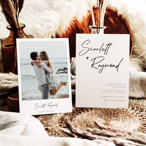 May include: Wedding invitation featuring a photograph of a couple embracing on a beach. The invitation is white with black text and reads "Scarlett + Raymond" and "August 25th 20XX".