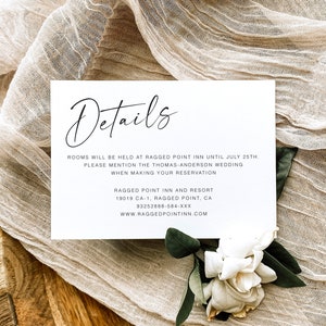 May include: A white card with black text that reads "Details" and provides information about a wedding. The text includes the name of the venue, the date, and contact information. The card is on a beige fabric background.
