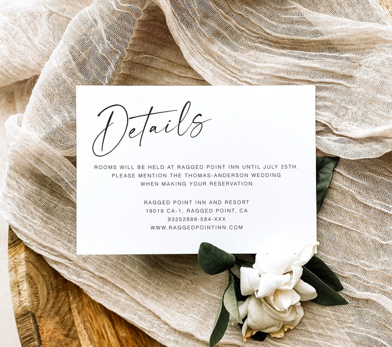 May include: A white card with black text that reads "Details" and provides information about a wedding. The text includes the name of the venue, the date, and contact information. The card is on a beige fabric background.