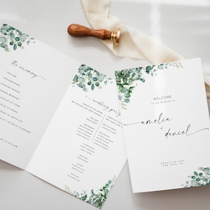 Könnte beinhalten: Hochzeitszeremonie-Programm mit grünem Eukalyptus-Blumendesign. Das Programm enthält die Reihenfolge der Zeremonie und eine Liste der Hochzeitsgesellschaft. Der Einband lautet "Willkommen zur Hochzeit von Amelia + Daniel".