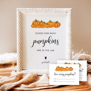 May include: A white frame with a sign that says "Guess how many pumpkins are in the jar? Good luck!" with a drawing of pumpkins. There are also two white cards with the text "How many pumpkins?" and a space to write a name and guess.