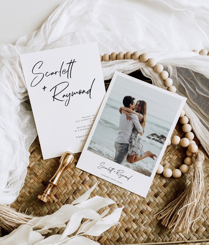 May include: Wedding invitation featuring a photograph of a couple embracing on a beach. The invitation is white with black text and reads "Scarlett + Raymond" and "August 25th 20XX".