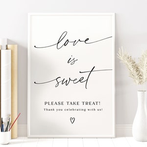 May include: A white sign with black text that reads "Love is sweet. Please take treat! Thank you celebrating with us!" with a small heart at the bottom.