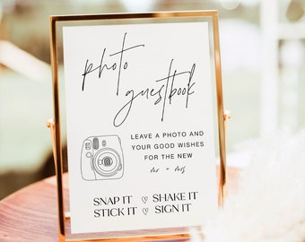 May include: A white sign in a gold frame with the text "photo guestbook" and instructions for guests to leave a photo and good wishes for the new Mr. and Mrs. The sign also says "Snap it, Shake it, Stick it, Sign it".