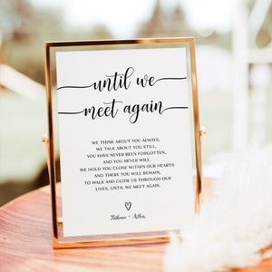 May include: A framed white sign with black text that reads "until we meet again". The text continues with a poem about remembering someone who has passed away. The sign is on a wooden surface with a white feather in the foreground.