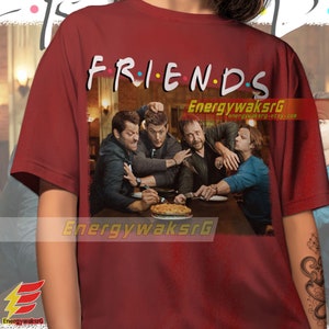 May include: Red t-shirt with a graphic print of four men sitting at a table with a pie. The text "FRIENDS" is above the image.