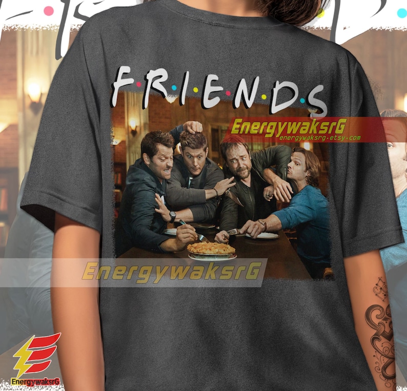 May include: A dark gray t-shirt with the word "FRIENDS" printed in colorful letters. The shirt features a graphic of four men sitting at a table with a pie in front of them. The graphic is in a vintage style.