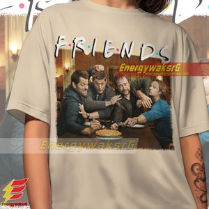 May include: A beige t-shirt with a vintage-style graphic of four men sitting at a table with a pie. The graphic includes the text "FRIENDS" with a black outline and colorful dots.