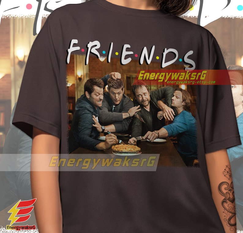 May include: A dark gray t-shirt with the word "FRIENDS" printed in colorful letters. The shirt features a graphic of four men sitting at a table with a pie in the center. The men are all wearing casual clothing and have serious expressions on their faces.