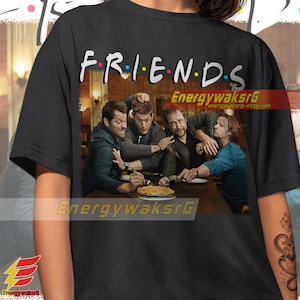 May include: Black t-shirt with a graphic of four men sitting at a table with a pie. The text "FRIENDS" is above the graphic.