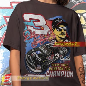 Pu&ograve; includere: Una maglietta marrone scuro con una grafica in stile vintage del pilota di auto da corsa Dale Earnhardt Jr. La grafica presenta un'auto da corsa nera con il numero 3, un ritratto di Earnhardt Jr. e il testo "Goodwrench" e "Seven Times Winston Cup Champion".