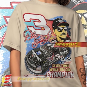 Pu&ograve; includere: Una t-shirt beige con una grafica in stile vintage di Dale Earnhardt, un pilota di auto da corsa, e la sua auto da corsa numero 3. La grafica include il testo "Goodwrench", "Seven Times Winston Cup Champion", e la firma di Dale Earnhardt.