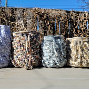 May include: Four crocheted drawstring bags in different colors: light blue, brown and white, blue, and beige. The bags are sitting on a wooden table.