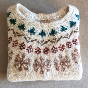 May include: Cream-colored sweater with a round neckline and intricate knit patterns. The design features teal, brown, and red floral and geometric motifs. The folded sweater is a cozy, warm garment.
