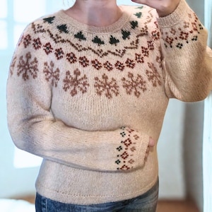 May include: Beige knit sweater with a round neckline and long sleeves. The sweater features a snowflake and geometric pattern in brown, green, and beige. The cuffs also have a geometric pattern. The sweater is a cozy, warm garment.