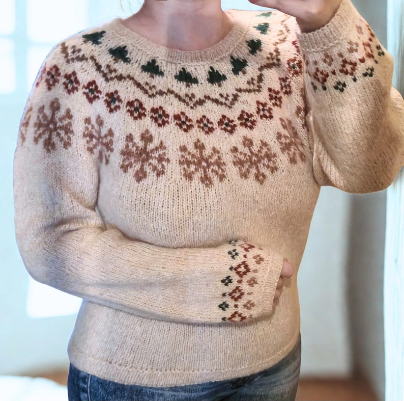 May include: Beige knit sweater with a round neckline and long sleeves. The sweater features a snowflake and geometric pattern in brown, green, and beige. The cuffs also have a geometric pattern. The sweater is a cozy, warm garment.