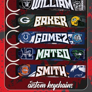 Op de afbeelding: Een verzameling op maat gemaakte sleutelhangers met teamlogo's en namen. De sleutelhangers tonen de logo's van de Raiders, Packers, Colts, Seahawks en Broncos, samen met de namen William, Baker, Gomez, Mateo en Smith. De tekst "custom keychains" is ook zichtbaar.