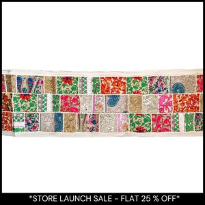 Peut inclure: Textile décoratif avec un motif patchwork. Les pièces rectangulaires présentent des motifs floraux et cachemire dans des tons de rouge, vert, or et rose. Les bords sont bordés de tissu blanc.