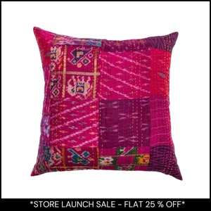 Puede incluir: Un cojín decorativo cuadrado con un diseño de patchwork en tonos rosa, magenta y morado. El cojín presenta varios patrones de tela y costuras doradas. El tema general es bohemio y ecléctico.
