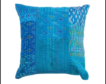 May include: Square, patchwork pillow in shades of blue. The pillow features a variety of fabric patterns and textures, with visible stitching in white and pink. The overall design is a mix of geometric and abstract shapes, creating a unique and handcrafted look.