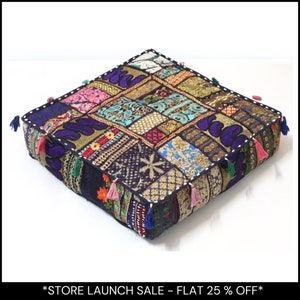 May include: Square floor cushion with a patchwork design in various colors, including purple, gold, and blue. The cushion has a black border with tassels in multiple colors. The text at the bottom says "STORE LAUNCH SALE - FLAT 25% OFF".