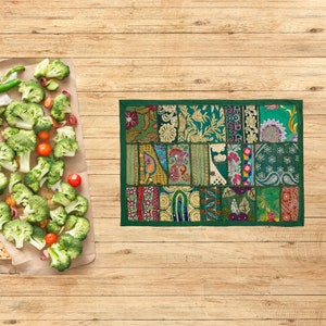 Könnte beinhalten: Ein rechteckiger Tischset im Patchwork-Stil mit grünem Rand. Das Tischset zeigt verschiedene gemusterte Stoffquadrate in Grün-, Gold- und anderen Farbtönen. Brokkoliröschen, Tomaten und anderes Gemüse liegen auf Backpapier.