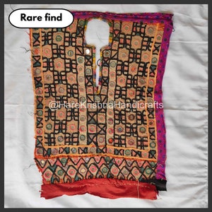 Puede incluir: Textil vintage con intrincados bordados y espejos. La tela beige está adornada con patrones geométricos en negro, naranja y verde, con un borde rojo y un ribete morado. El texto "Rare find" está en un óvalo blanco.