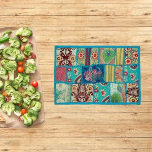 Könnte beinhalten: Rechteckiger Patchwork-Textil mit türkisfarbenem Rand. Der Patchwork weist verschiedene Blumen- und Paisley-Muster in Türkis-, Rot- und Goldtönen auf. Brokkoliröschen, Kirschtomaten und grüne Paprika sind auf einem braunen Papier angeordnet.