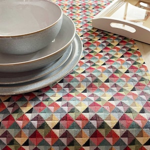 May include: A set of four grey ceramic bowls with a subtle speckled texture. The bowls are stacked on top of each other and are sitting on a colourful geometric table runner.
