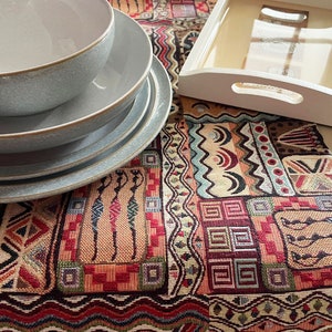 May include: A set of four grey ceramic bowls with a textured finish, arranged on a colourful woven tapestry with geometric patterns.