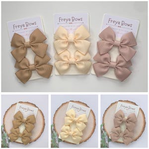 May include: Three sets of hair bows in beige, cream, and light pink. Each set includes two bows, with the text "Freya Bows Handmade with Love" on the card.