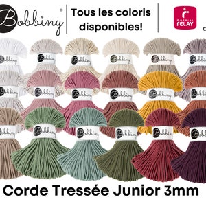 Peut inclure: Assortiment de couleurs de corde tressée junior de 3 mm, disposées en forme de pyramide. La corde est en coton et disponible dans une variété de couleurs, notamment le blanc, le beige, le rose, le rouge, le jaune, le vert et le marron. Le texte "Corde Tressée Junior 3mm" est imprimé sous la corde.