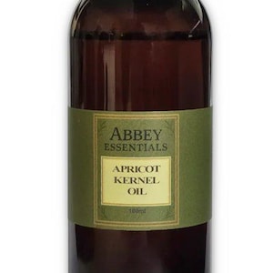 Op de afbeelding: Een bruine glazen fles Abbey Essentials Abrikozenpitolie. De fles heeft een zwarte dop en een groen etiket met witte tekst. De fles bevat 100 ml olie.