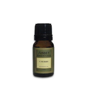 Op de afbeelding: Een kleine, bruine glazen fles Abbey Essentials Cherry geurolie. Het etiket toont de merknaam en het woord "CHERRY" in een rechthoekige doos. De fles heeft een zwarte dop en bevat 10 ml olie.