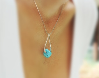 Puede incluir: Un collar de cadena de plata con un colgante de piedra turquesa. El colgante está sujeto en un bucle de plata.