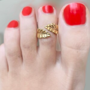Può includere: Anello per dita dei piedi in oro con un design a foglia. L'anello è indossato sul secondo dito del piede di un piede con smalto rosso.