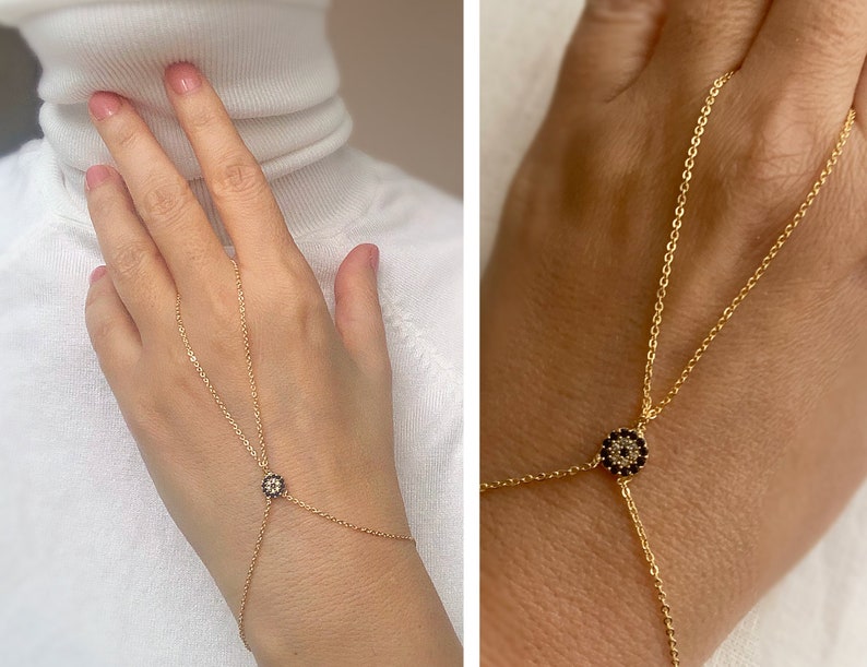 May include: A gold chain bracelet with a black and white evil eye charm. The bracelet is adjustable and can be worn on the wrist or as a hand chain.