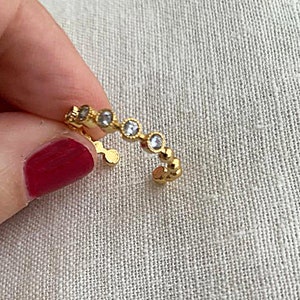 May include: A gold ring with a row of small, clear stones. The ring is open and has a simple design.