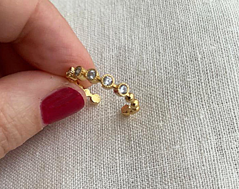 May include: A gold ring with a row of small, clear stones. The ring is open and has a simple design.