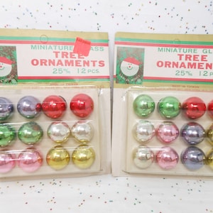 May include: Two packages of miniature glass Christmas tree ornaments. Each package contains 12 ornaments in various colors, including red, green, silver, pink, purple, and gold. The packaging reads "Miniature Glass Tree Ornaments".