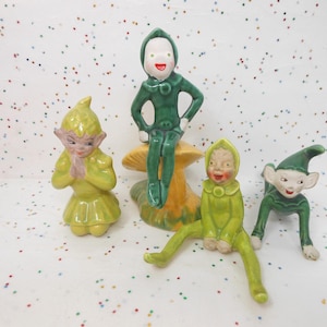 May include: Four ceramic figurines of elves, two are green and two are yellow, with green accents. One elf is sitting on a mushroom.